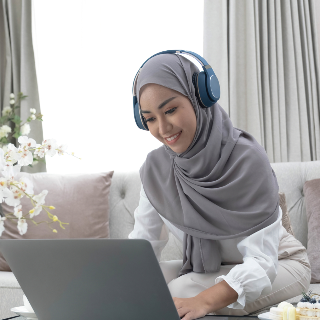 A woman in a hijab and headphones works on her laptop, illustrating the online tutoring experience offered in the UAE